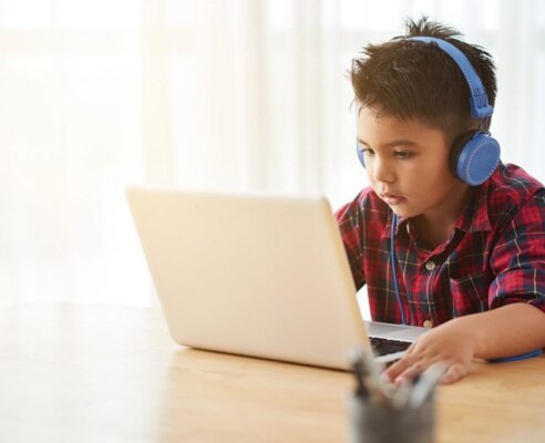 Young child learning on a laptop wearing blue headphones
