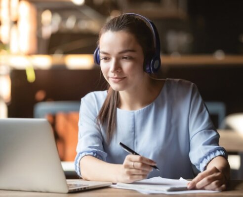 Woman learning remotely on her laptop wearing headphones at a coffee shop
