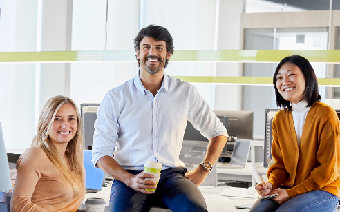 staff team sitting in chairs and on desk and smiling at camera
