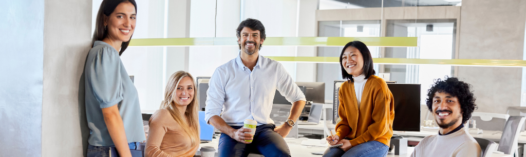 staff team sitting in chairs and on desk and smiling at camera