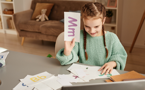 Girl holding up letters to computer during tutoring session