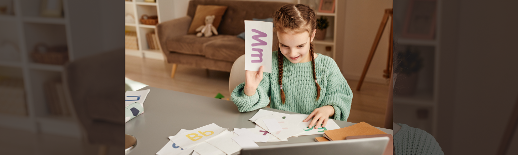 Girl holding up letters to computer during tutoring session