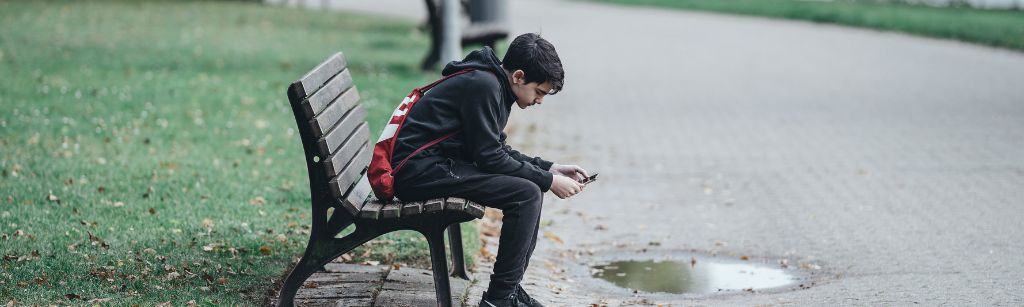 boy on bench in park looking at phone