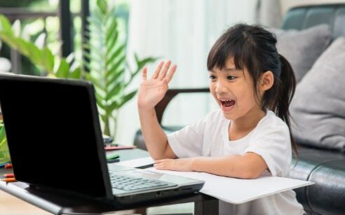 girl looking at computer and waving with a smile on her face