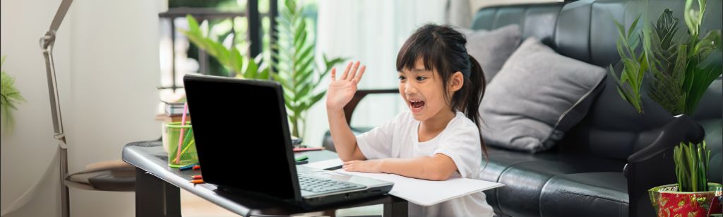 girl looking at computer and waving with a smile on her face