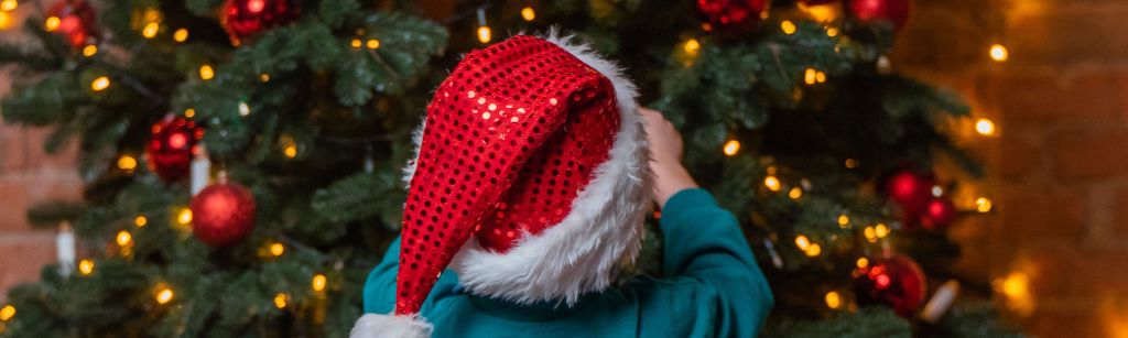 child in red hat decorating a christmas tree